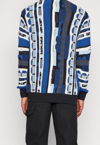 Strickpullover in Blau, Schwarz und Weiß mit geometrischem Muster. Verfügt über strukturierte Streifen sowie gerippte Bündchen und Saum. Legere Passform.