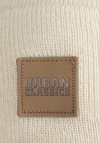 Krém színű kötött anyag, textúrált felülettel. Jellemzője egy barna bőrcímke, amelyen sötét betűkkel az "URBAN CLASSICS" felirat látható, körben varrással kiemelve.