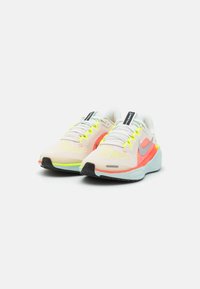 Zapatillas de running ligeras con parte superior de malla en blanco y coral, acentos neón, suela acolchada y suela exterior de goma negra.
