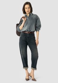 Chemise en denim gris délavé, coupe ample avec fermeture à boutons, associée à un jean en denim foncé avec des ourlets roulés. Accessoirisée avec une ceinture tressée et des talons à motifs.
