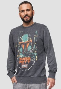 Sudadera gris con un gran gráfico de Boba Fett, con acentos en naranja y turquesa. Los puños y la cintura acanalados aportan textura.