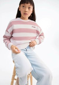 Felpa a righe rosa e bianca, con polsini e colletto a costine, con la scritta "Dreamer" ricamata in rosso. Abbinata a jeans azzurri chiari.