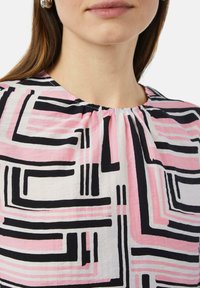 Witte blouse met lange mouwen en geometrisch patroon, voorzien van opvallende zwarte en roze lijnen. Gerimpelde halslijn en lichte stoftextuur.