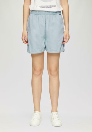 Helle blaue Shorts mit elastischem Bund und umgeschlagenen Säumen. Leichter Stoff, lockere Passform, gewebte Textur. Weiße Turnschuhe, die zu den Shorts getragen werden.