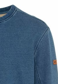 Felpa in denim blu con scollo rotondo, tessuto testurizzato e un piccolo logo in pelle marrone sulla manica sinistra.