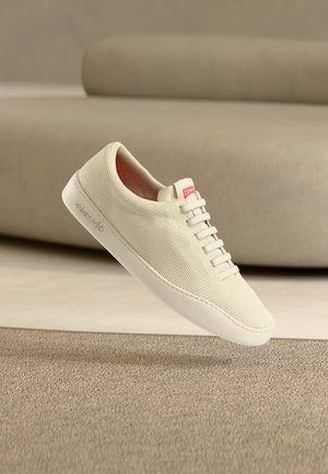 Hellbeiger Sneaker mit strukturiertem Strick-Obermaterial, weißer Gummisohle und pinkem Logo-Akzent. Verfügt über sechs Schnürsenkel-Ösen und ein minimalistisches Design.