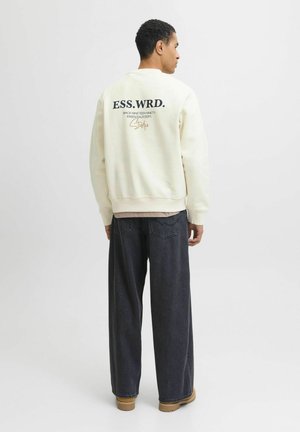 Cream-colored sweatshirt featuring "ESS.WRD." text on the back, paired with loose-fitting dark jeans and tan boots. Smooth fabric texture.