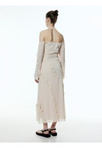 Lichtroze off-shoulder jurk met ruffles, lange mouwen en een geknoopte halslijn. Heeft een vloeiende silhoët die tot halverwege de kuit reikt. Zwarte sandalen.