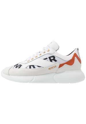 White mesh and leather sneaker features black lettering, gold accents, and an orange design element on the heel. Thick white sole.