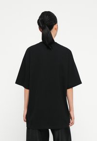 Camiseta negra de gran tamaño con mangas cortas, hecha de algodón suave. Presenta un escote redondo y un ajuste relajado, con aberturas laterales en el dobladillo.