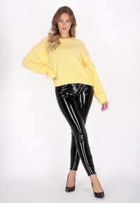 Pulover galben tricotat cu o suprafață texturată și embellishments, combinat cu colanți lucioși din piele sintetică negri, completat cu tocuri negre.