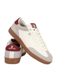 Zapatillas de cuero blancas con acentos de ante gris, lengüeta trasera roja, suela de goma y un logotipo. Presentan cordones finos y perforaciones en los laterales.