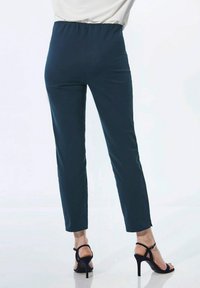 Marineblauwe, enkellange broeken met een gathered elastische tailleband, een gladde textuur en een slim fit, gecombineerd met zwarte hoge hakken.