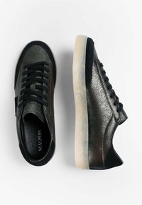 Par de zapatillas bajas negras y plateadas con purpurina, con cordones negros y suelas de goma blanca texturizada sobre un fondo blanco.