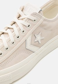 Beige mockask Converse All Star sneakers med vita snören, stjärna och chevron-logotyp, och strukturerad vit gummisula.