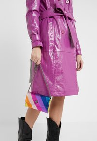 Glanzende paarse handtas met krokodillenprint, voorzien van een meerkleurig gestreept ontwerp, met een zilveren kettingriem en een decoratieve sluiting.