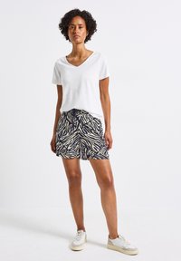 Vit t-shirt med v-ringad hals, parat med shorts i zebramönster i marinblått och krämfärgat. Modellen bär vita sneakers. Mjuk tygkvalitet, avslappnad passform.