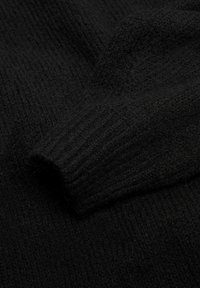 Černý pletený svetr s texturovaným, žebrovaným povrchem a měkkým, teplým vzhledem. Látka je nadýchaná s mírným leskem.