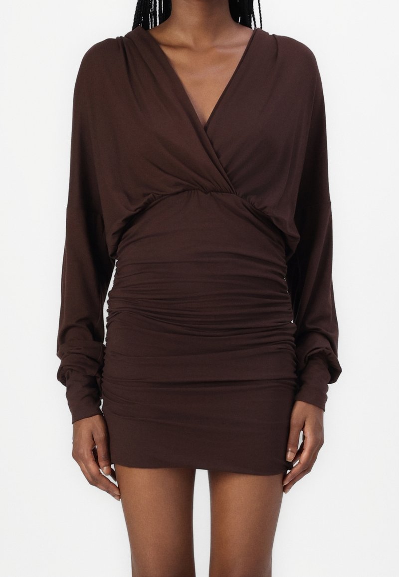 Robe-pull marron à manches longues, devant croisé et texture froncée à la taille. Tissu lisse avec une coupe ajustée.