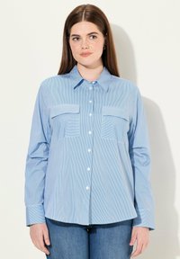Camicia button-up a manica lunga di colore blu chiaro con strisce verticali bianche, dotata di due tasche sul petto e colletto classico. Materiale in misto cotone.
