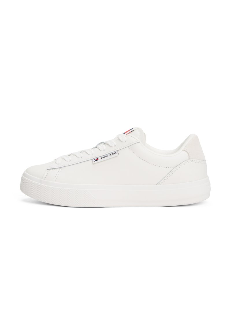 Vit sneaker med en slät läderöverdel, platt snörning och texturerad gummisula. Har en liten logotag på sidan.
