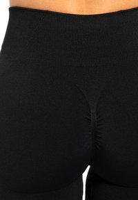 Leggings noirs taille haute avec une texture lisse et extensible. Présente un léger drapé à l'arrière et une taille côtelée.