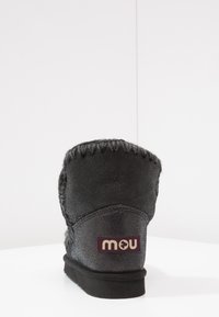 Zwarte suède enkellaars met een gestructureerd oppervlak, contrasterende stiksels en een rubberen zool. Heeft een logopatch op de hiel.