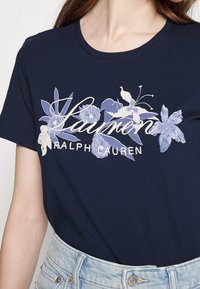 Námořnická modrá bavlněná tričko s květinovým potiskem ve světle modré a bílé barvě, s nápisem "Lauren Ralph Lauren" v kurzívě.
