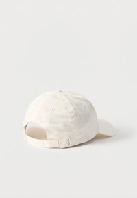 Μπεζ ποδοσφαιρικό καπέλο από βαμβάκι, εμφανιζόμενο από πίσω με ρυθμιζόμενο λουράκι και μεταλλικό πόρπη σε απλό λευκό φόντο.