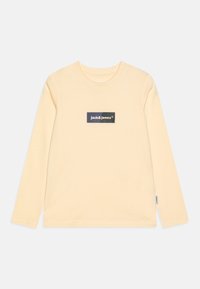 Langermet t-skjorte i lys gul, laget av mykt stoff, med et rektangulært etikett i marineblått med "Jack & Jones" tekst på brystet.