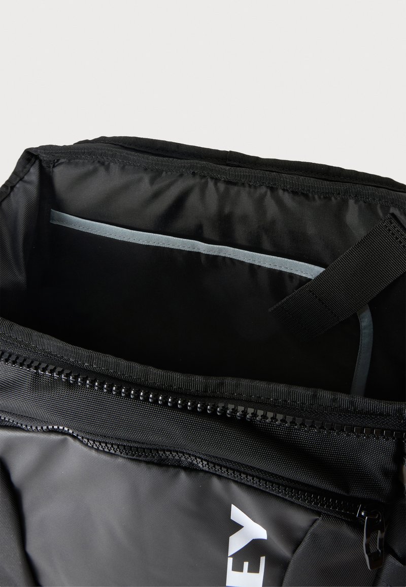 Schwarze Tasche mit Reißverschluss und offenem Hauptfach, das einen grauen inneren Trenner und einen schwarzen Riemen innen zeigt.