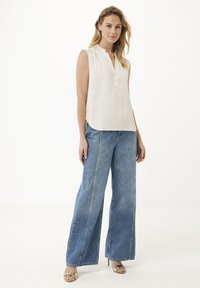 Ljusfärgad ärmlös blus med en knappslå och sidofickor, parat med vida denimjeans, som har kontrasterande sömmar och en avslappnad passform.