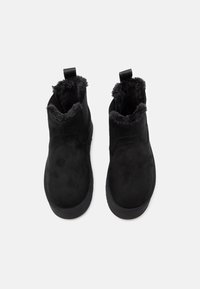 Pair of black suede ankle boots with thick fur lining and pull tabs, shown from above on a light background.