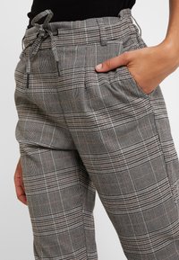 Grå rutiga byxor med avslappnad passform, dragsko i midjan, sidofickor och subtila detaljer i ett rutig mönster.