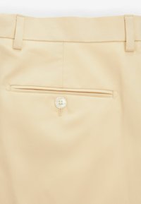 Nahaufnahme einer beigen Stoffhose mit einer Gesäßtasche, einem kleinen Knopf und Gürtelschlaufen am Bund.