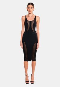 Schwarzes, tailliertes Midi-Kleid mit transparenten Einsätzen, geschwungenen Ausschnitten und dünnen Trägern. Glatte Textur mit körperbetontem Design, ergänzt durch Riemchenheels.