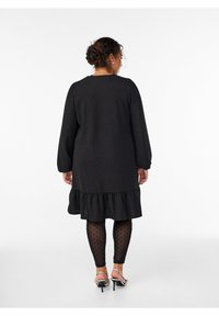 Čierne šaty s volánom, štruktúrovanou látkou a dlhými rukávmi. Oblečené s čiernymi legínami s bodkami a striebornými sandálmi na podpätku.