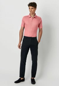 Hemdkleur met korte mouwen, knoopsluiting in textuur lichtroze, gecombineerd met donkere broeken. Schoeisel bestaat uit donkere suède instappers.