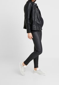 Svart läderjacka, slimfit svarta byxor och ljusgrå sneakers. Jackan har dragkedja och sidofickor; byxorna har en slät textur.