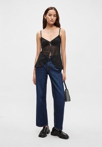 Melns caurspīdīgs tops ar centrālu sudraba gredzena detaļu, kopā ar augstās jostasvietas zilām džinsa biksēm un melniem apaviem. Mazs melns rokassomiņa.