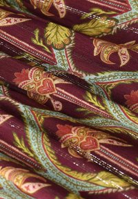 Tissu bordeaux présentant des motifs floraux et de feuilles en jaune et rose, avec des accents bleu clair détaillés et un léger éclat.