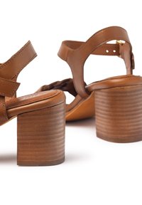 Sandales à talons en cuir marron, avec un large bloc de talon texturé et une sangle de cheville réglable. La conception à bout ouvert présente des accents tressés.