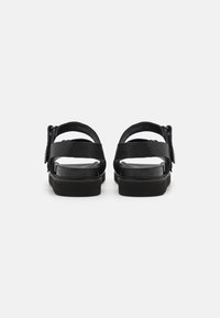 Sandales noires avec deux larges sangles, boucles ajustables et une semelle plate au fini texturé. Design épuré et minimaliste.