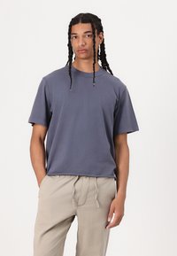 T-shirt à manches courtes et col rond de couleur bleue douce, fabriqué en coton. Il présente une coupe décontractée et une texture lisse. Associé à un pantalon beige clair.