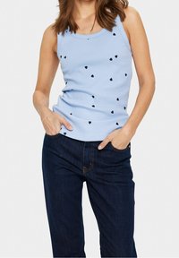 Ljusblå ribbad linne med spridda svarta hjärtan, ihopparad med mörka denimjeans. Linne har rund halsringning och enkla axelband.