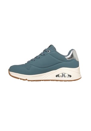 Blauer Sportschuh mit weißer dicker Sohle, transparentem Luftpolster, silbernem Fersenakzent und blauen Schnürsenkeln auf einem hellbraunen Profil.