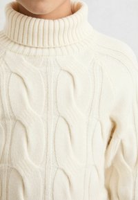 Suéter blanco de punto trenzado con cuello alto acanalado y patrones texturizados. Tejido de punto suave con una apariencia cálida y acogedora.