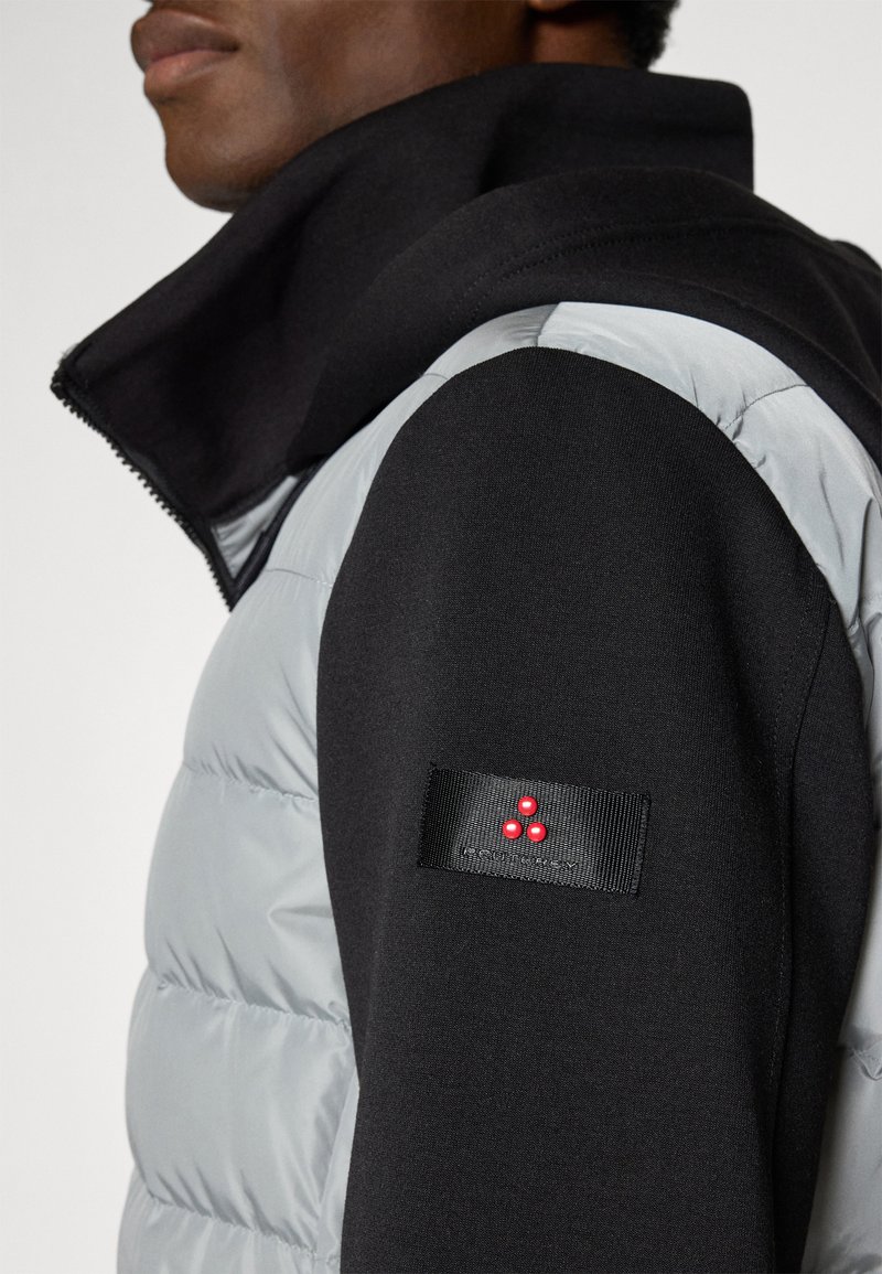 Puchowa kurtka z szarym tułowiem i czarnymi rękawami, z wysokim kołnierzem i naszywką z logo na rękawie, podkreślona czerwonymi akcentami.