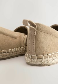 Espadrilles de ante beige sin cordones con suela de cuerda y detalles de costura; cuentan con un pequeño lazo en el talón para facilitar su uso.