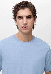 Ljusblå bomullströja med rund halsringning och korta ärmar. Slät textur och enkel design utan mönster eller utsmyckningar.